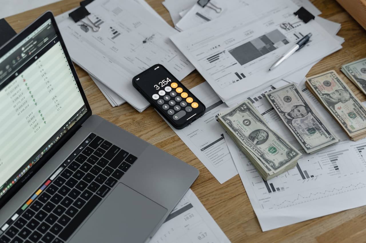 abstract graphic with dollar bills, laptop, calculator, and papers on a desk